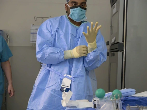 A health care worker in full personal protective equipment (PPE), including a surgical mask, gown, and gloves, prepares to administer care.