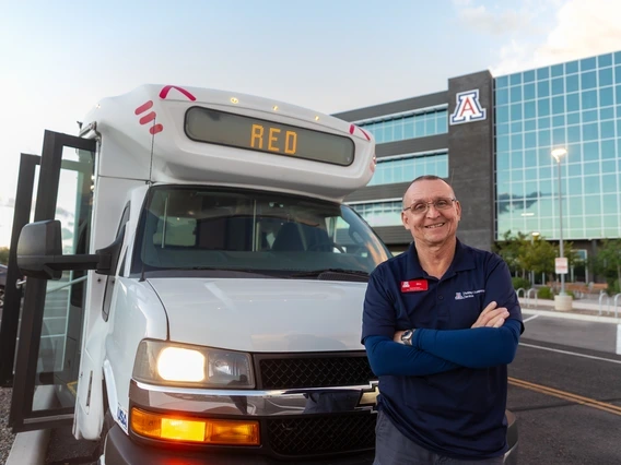 Bill Mason standing outside a Cat Tran shuttle near a building in the background with a Block A logo on it