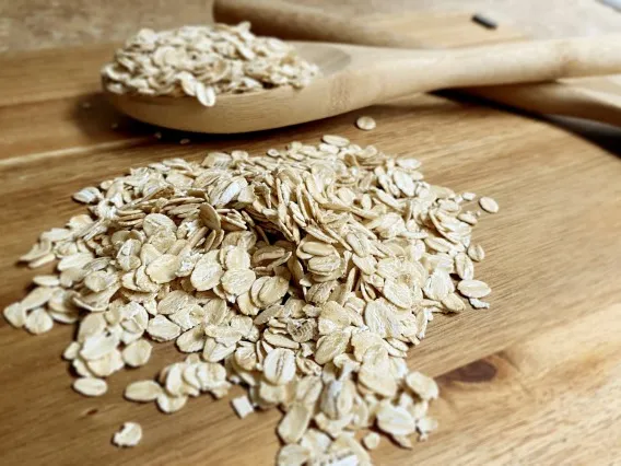 A wooden spoon rests on a wooden table next to a pile of uncooked oats.