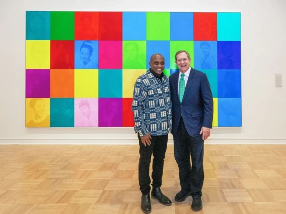 two men standing in front of a work of art depicting people's faces in colored squares