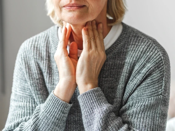 a closeup of the torso on an older adult who is lightly touching their own neck with both hands