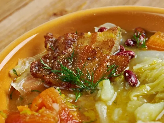 A close up of a stew containing meat, vegetables and beans