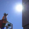 a construction worker standing on a lift near a building in the direct midday sun