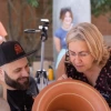 Eleni Hasaki looking over the shoulder of Roberto Paolini, an artist, to look at a reddish-colored vase that Paolini is painting a design on